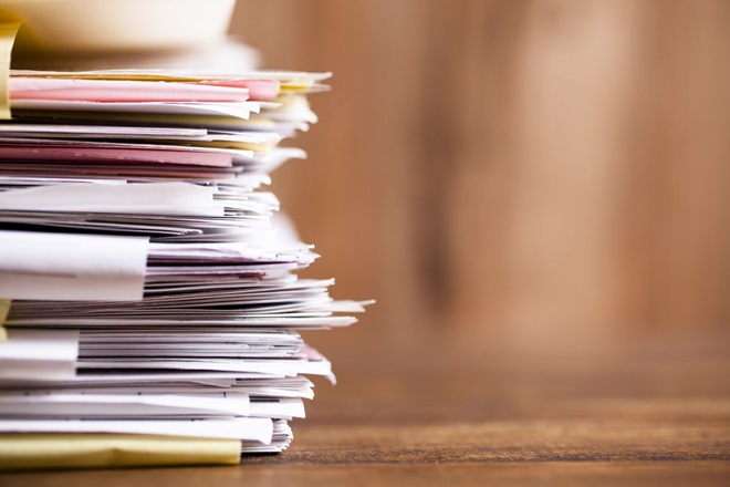 Large stack of multi-colored files and paperwork lie on an office desk.