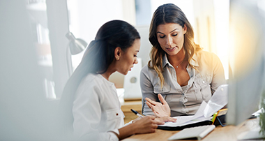 Two people talking over paperwork on a table