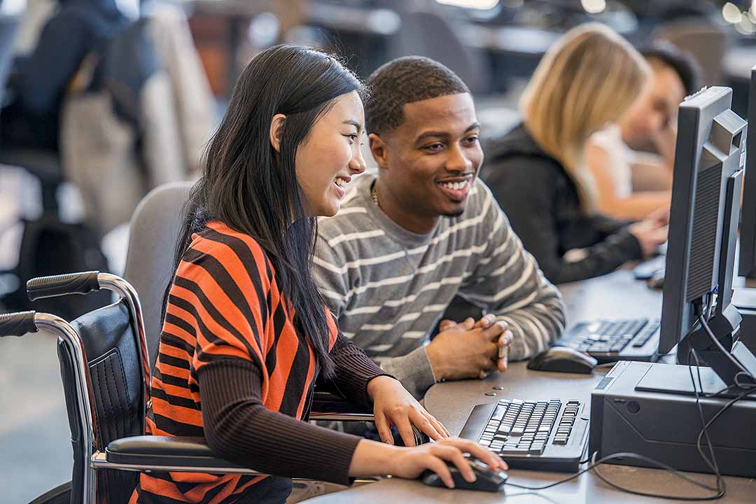 A student in a wheelchair with another student working on a computer together