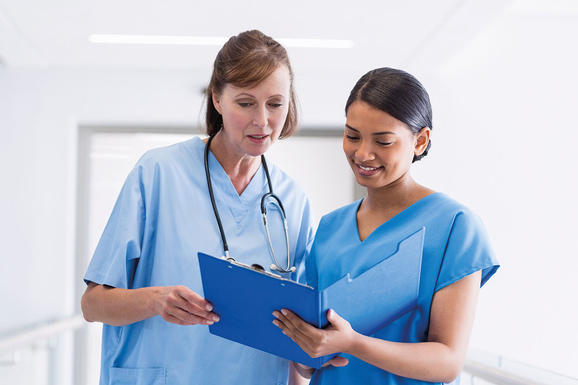 Two female medical professionals standing and discussing work on a clipboard