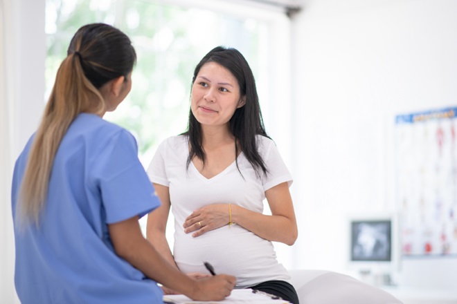 A female doctor in conversation with a pregnant women in a medical setting.