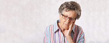Older woman with short grey hair wearing glasses and a striped shirt, resting her head on her hand.