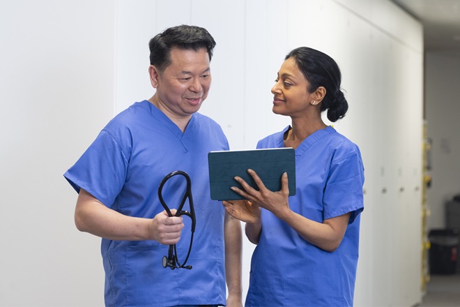 Two associate colleagues in blue scrubs talk with a tablet