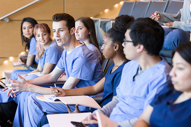A group of students in a lecuture theatre, wearing scrubs