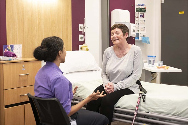 A patient sat on a bed talking to a doctor sat on a chair. 