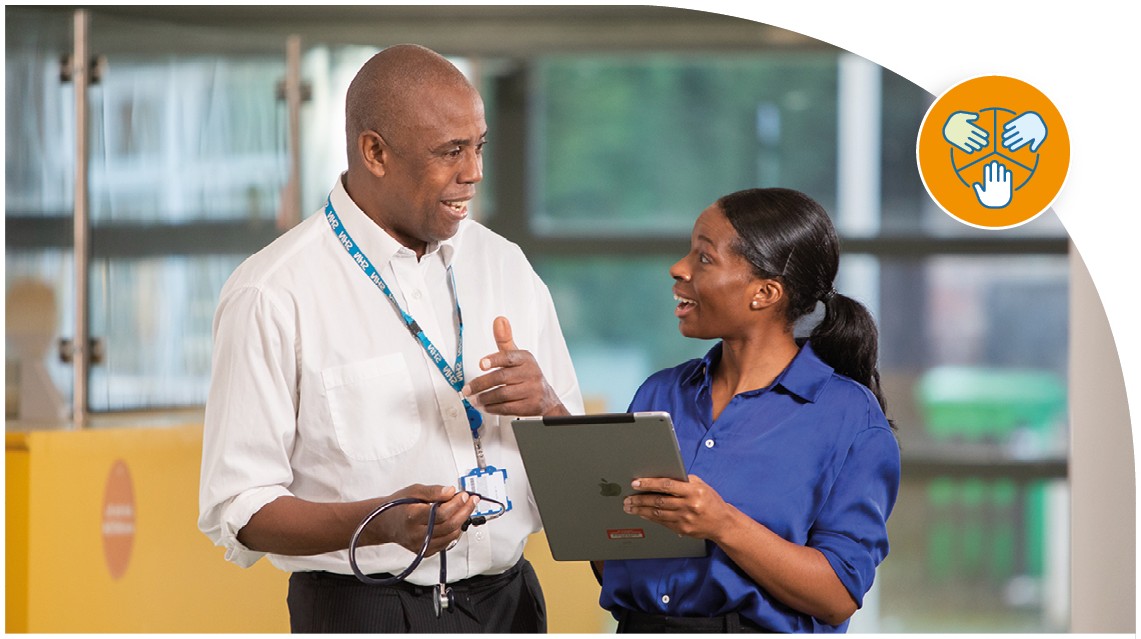 Two people stood in conversation looking at an ipad.