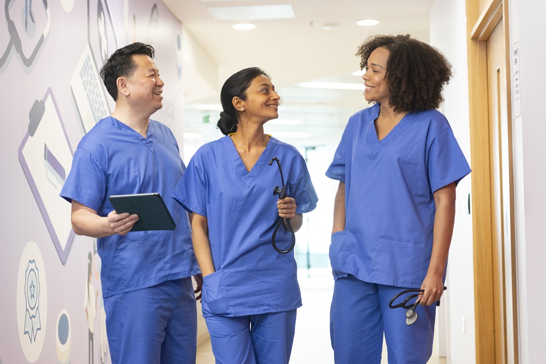 Three doctors in scrubs talking in a hallway